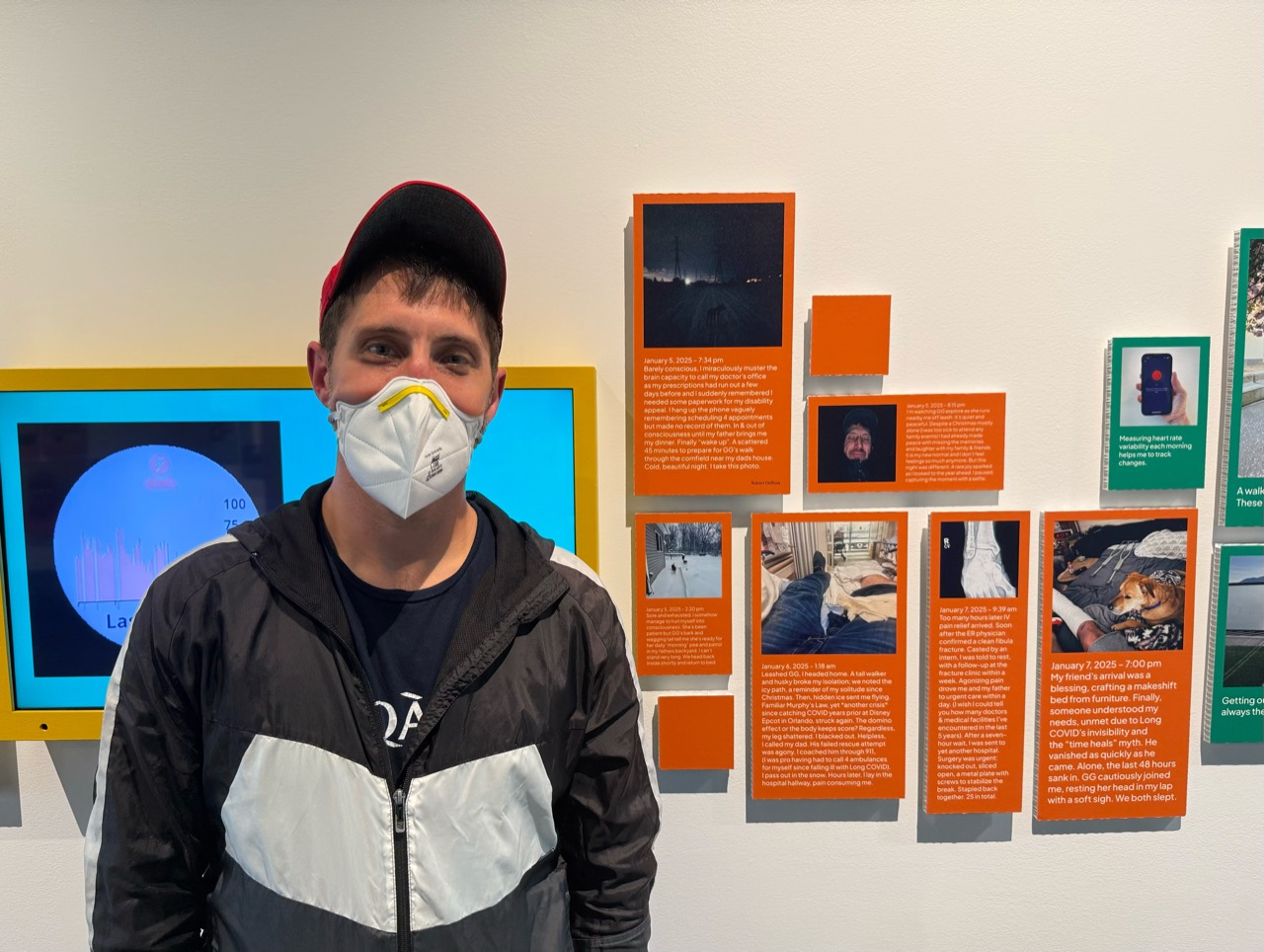 Robert DeRosa wearing a respirator beside the Living with Long COVID exhibition displays at the Museum of Vancouver.